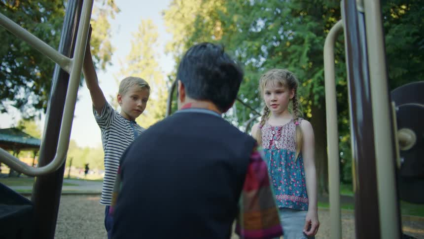 Sitting man and two blond children talking to him outdoors in the park and forest