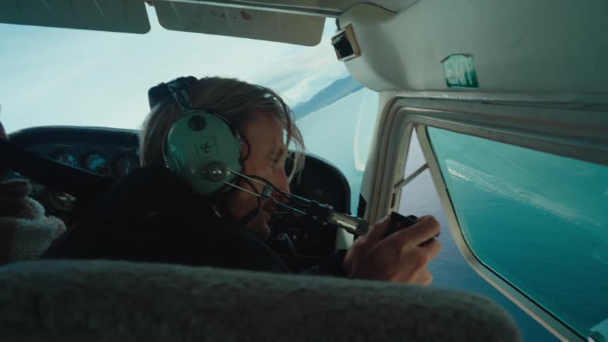 A man in a small plane takes pictures of the ocean and coast through an open window