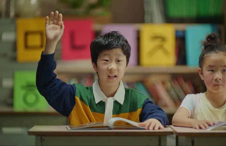 Student sitting at desk raises his hand at the classroom