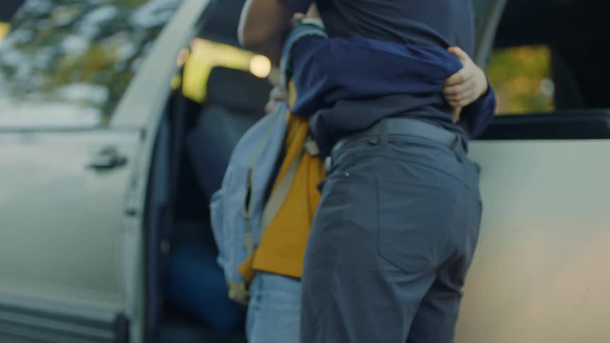 Setting sun shines through car as son rushes forward to hug father