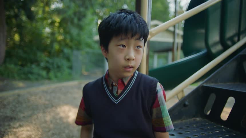 A young boy sitting on a play structure begins to fearfully back away