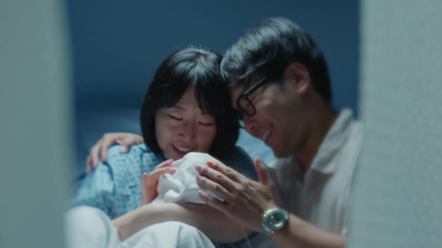 Father kisses mother as she holds their child while in hospital