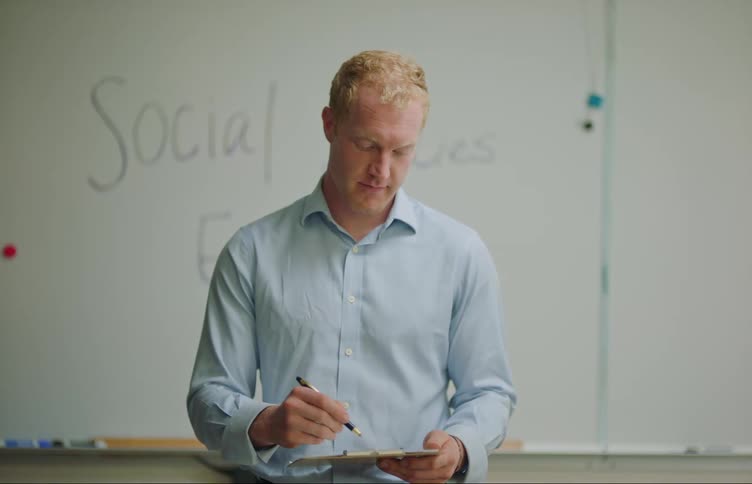 Teacher in a classroom taking notes with a pen in a notebook and having a conversation