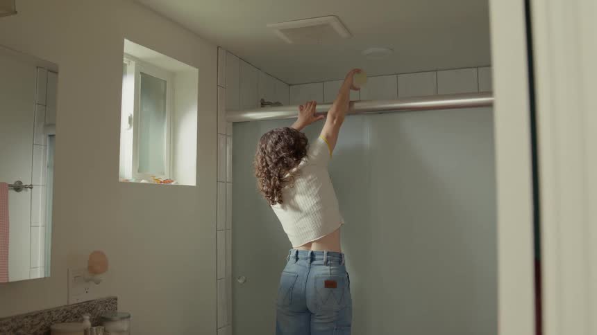 Woman with curly hair white shirt and jeans pulls a prank on man having a shower in the bathroom