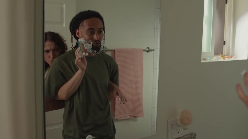 A girl is having fun shaving her boyfriend in the bathroom
