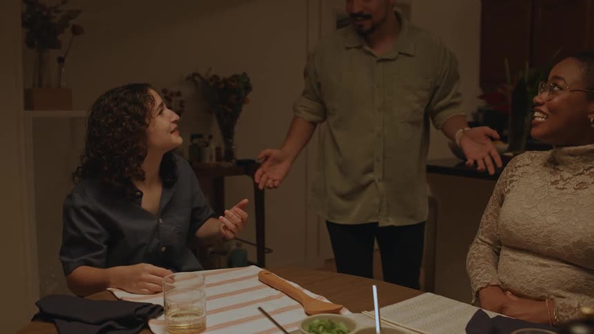 Two women sit at a table man clear bowls and laughs