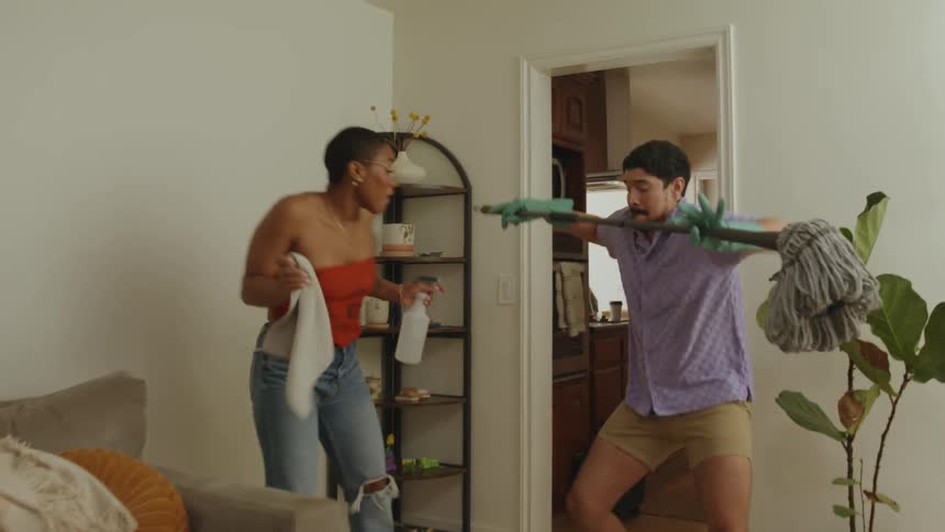 Man and woman dance indoors while cleaning