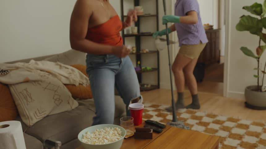 Couple dances while moping floor in living room with coffee table strewn with snacks