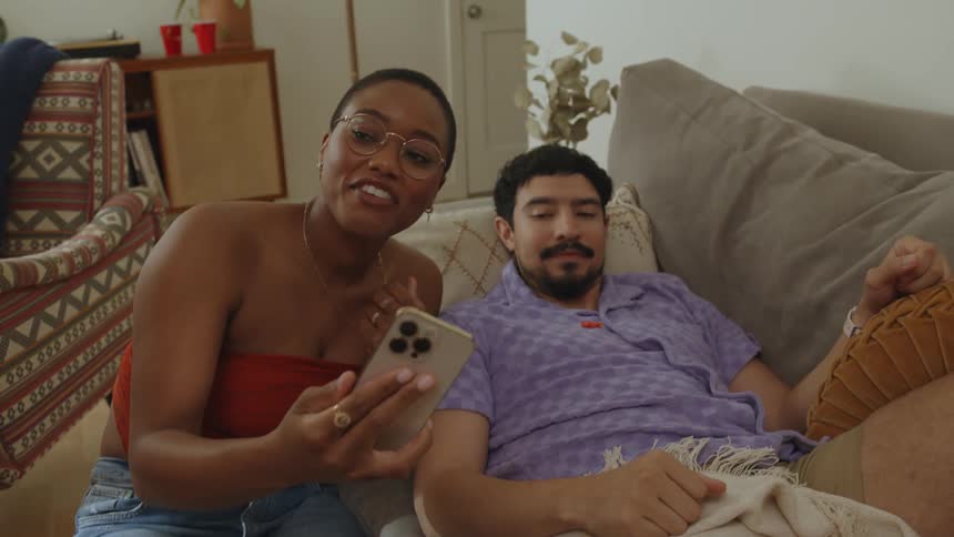 Woman smiles while she takes a selfie with man and talks to a third person