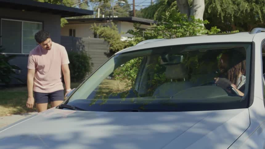 A man in a car talks to his friend on the street then gives him a ride