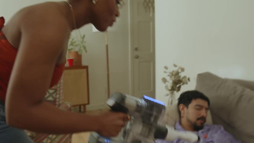 Man sleeping on a sofa while the woman cleans the house