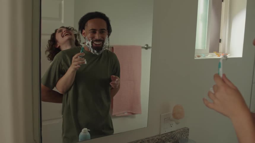 A man is shaving as a woman laughs