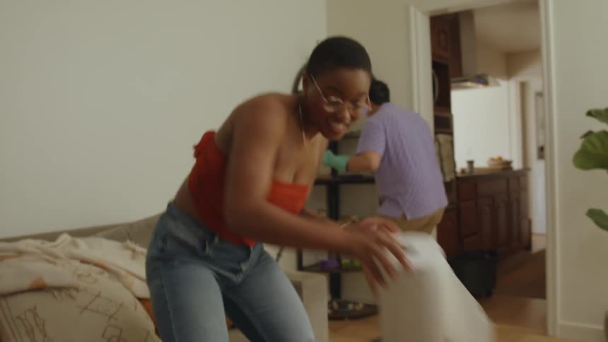 A man and a woman are cleaning a room and the woman is dancing as she cleans