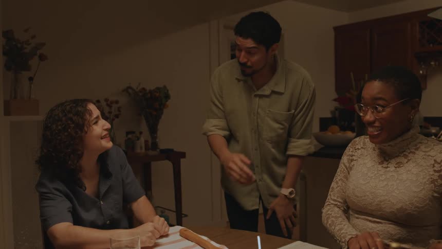 Two women sitting down and a man standing up say something funny and pick up two bowls from the table and everyone laughs