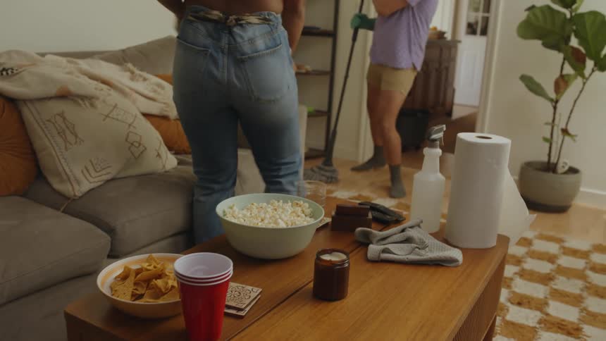A man and a woman are cleaning a room and dancing with a broom and gloves in their hands