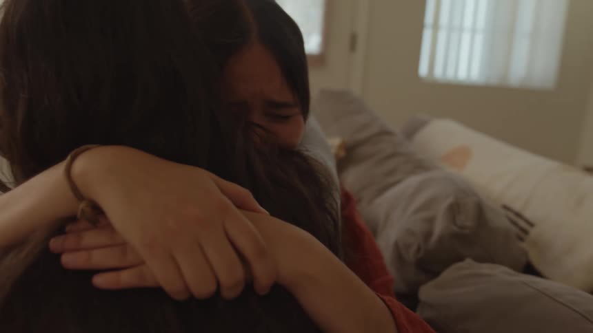 Woman hugs and consoles a friend crying in the couch at home