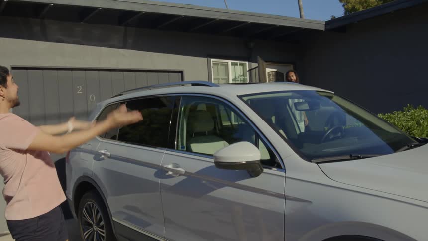 Man with dreadlocks and beard and his friend with pink t shirt and shorts get in car in front of house