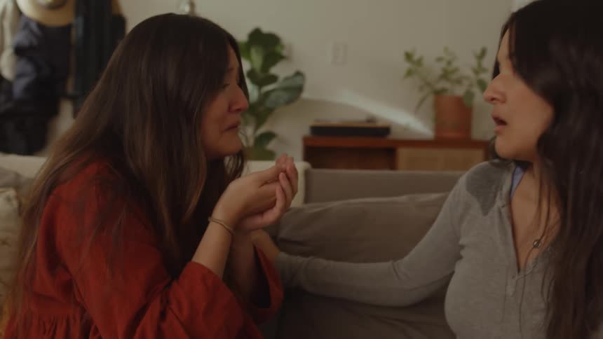 Two women sitting on the couch laughing and crying simultaneously deeply moved