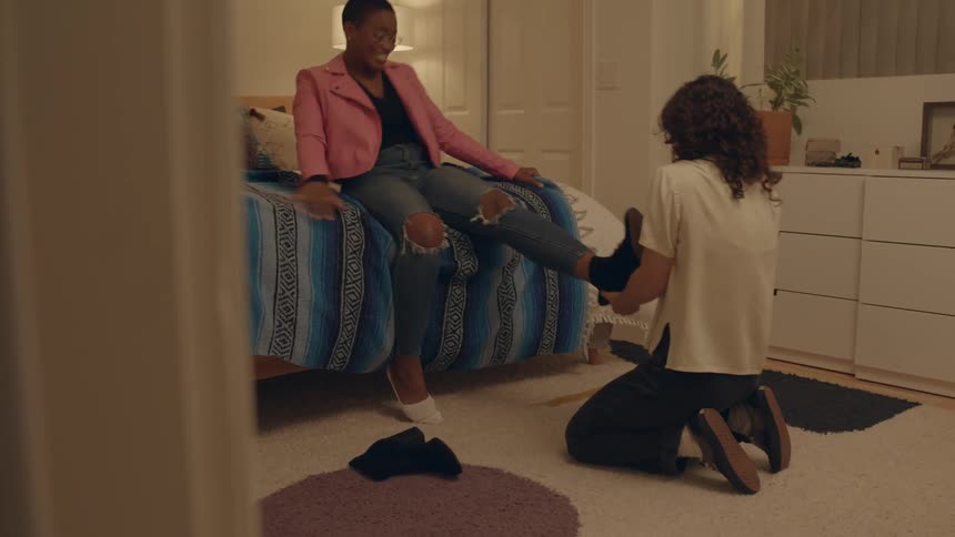 Girlfriends trying to get their boots off their feet in a bedroom