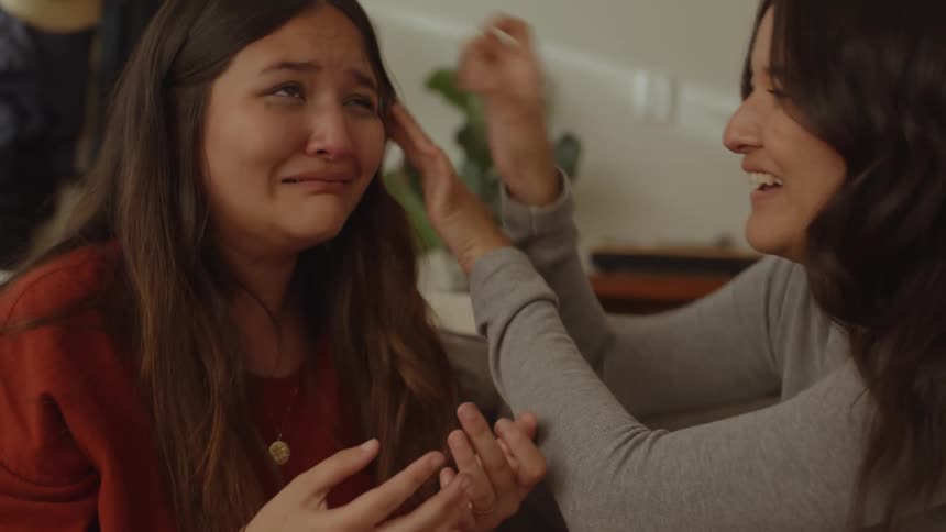 Two friends sitting on the couch with one of them crying and the other laughing both happy and emotional
