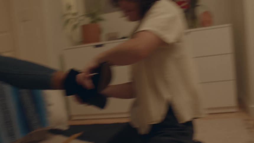 A young woman is helping another woman remove a pair of tight boots while sitting in a bedroom