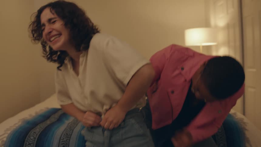 Girlfriends trying to put on jeans in a bedroom