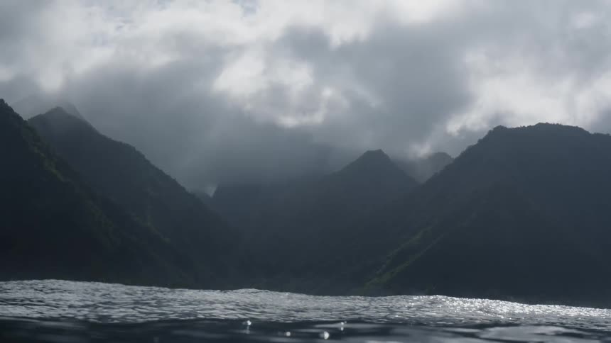 View of the moving sea with mountains covered in vegetation in the background