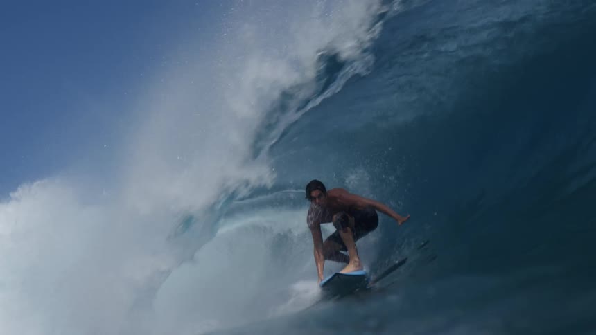 Young man rides a wave with a surfboard under a blue sky