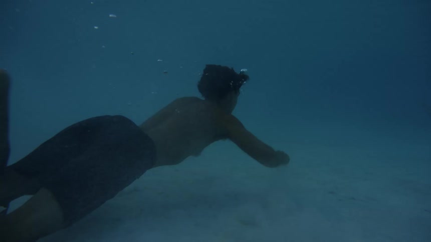 Man swimming underwater on the ocean close to the ocean floor passing by a swimming fish