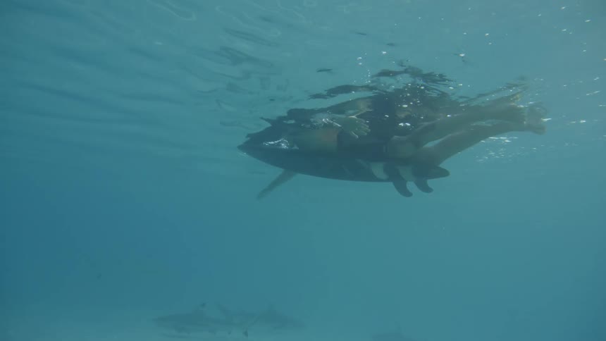A man swims while laying on a surfboard at midday
