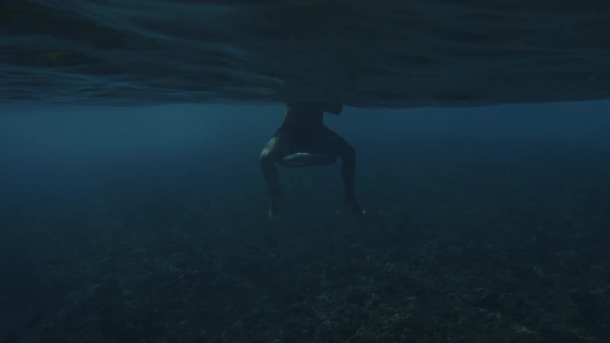 View from inside the sea with the legs of a person sitting on a surfboard