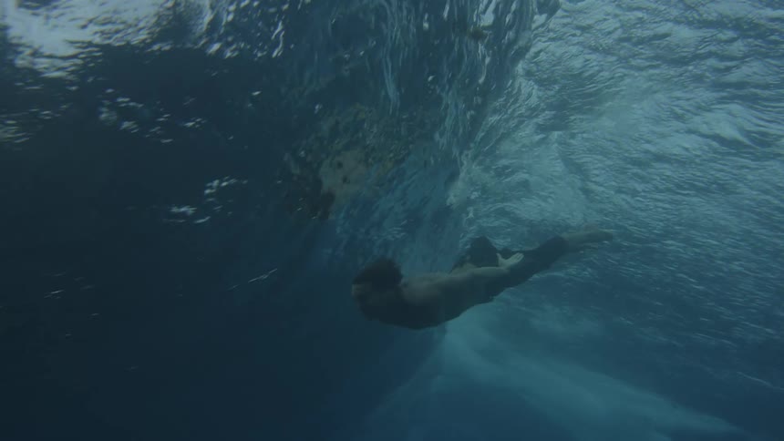 A man is underwater swimming beneath a large wave