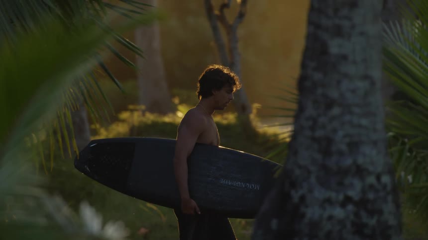 A man walking carrying his surfboard under one arm