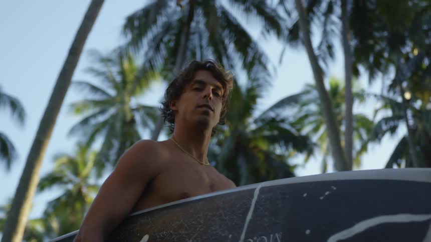 Surfer holding his surfboard in an outdoor setting with a palm tree biome