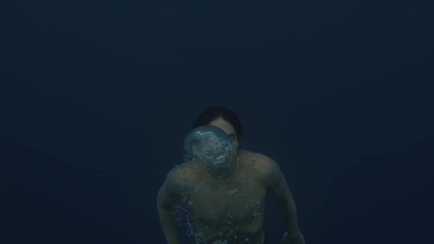 A young man underwater resurfacing and blowing bubbles with his mouth