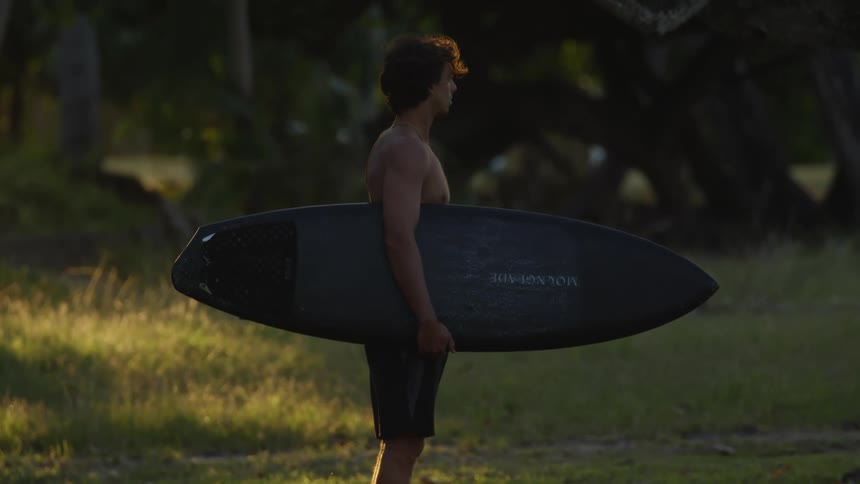 A man holding a surfboard with one hand and observing nature