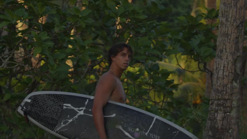 A man walking in the woods with a surfboard on his arm
