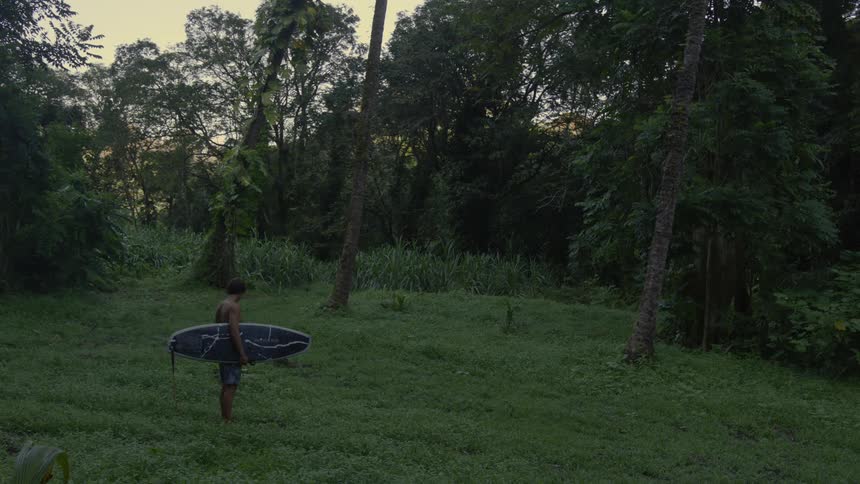 Man holding a surfboard between his arms on one side in the midst of nature