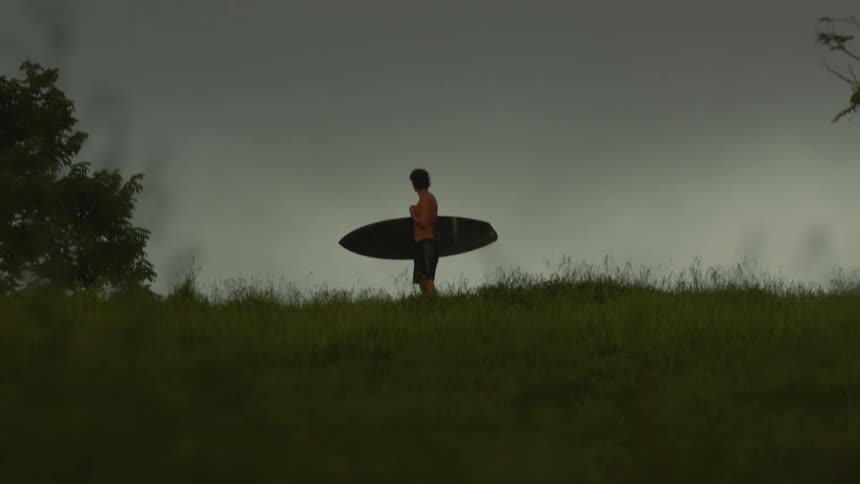 A surfer holding his board standing in a grass field
