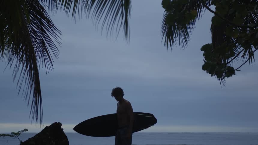 Man holding his surfboard in a natural environment with the sea in the background