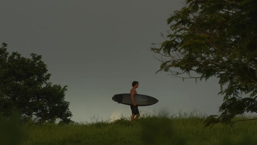 A man is holding his surfboard on the field