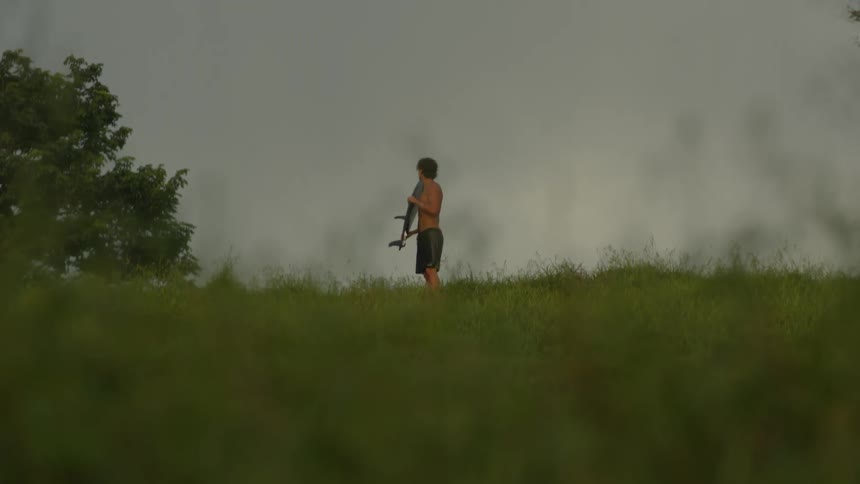 A man stands in a grassy field with a surfboard