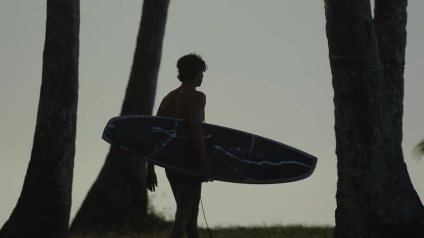 A man walks with a surfboard on the beach at sunset