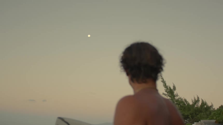 Shirtless man with a surfboard watching the sunset in a natural environment