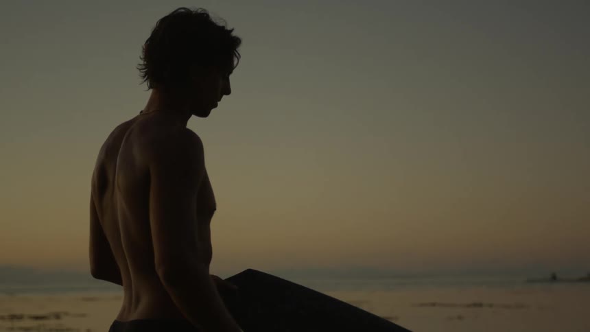 A man holding a surfboard on the beach at dusk