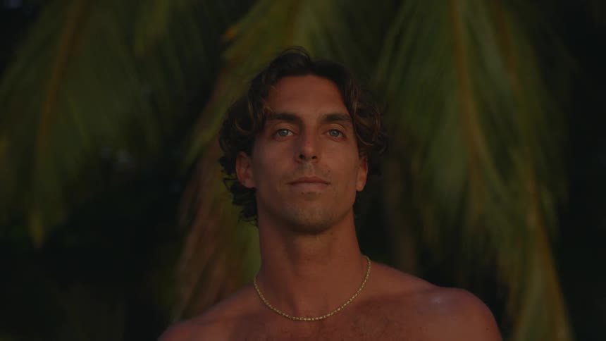 A shirtless man in chains with closed eyes slowly opens them