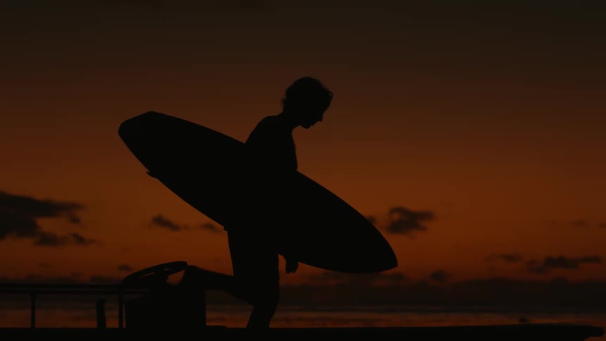 A man is carrying his surfboard by the shore