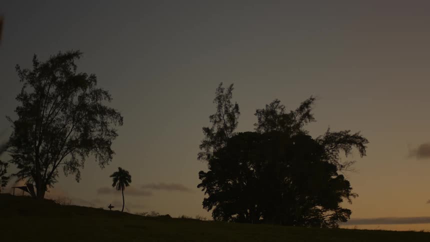 Dawn in a tropical region with a person walking in the background carrying a surfboard
