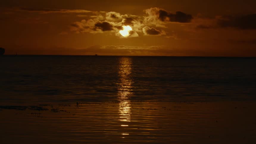 At sun down the dim lit sun is covered is cloud as it faintly shines on the surface of the sea