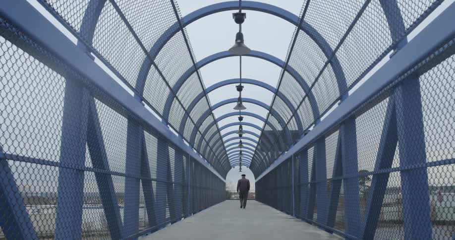A man walks on a fenced in bridge